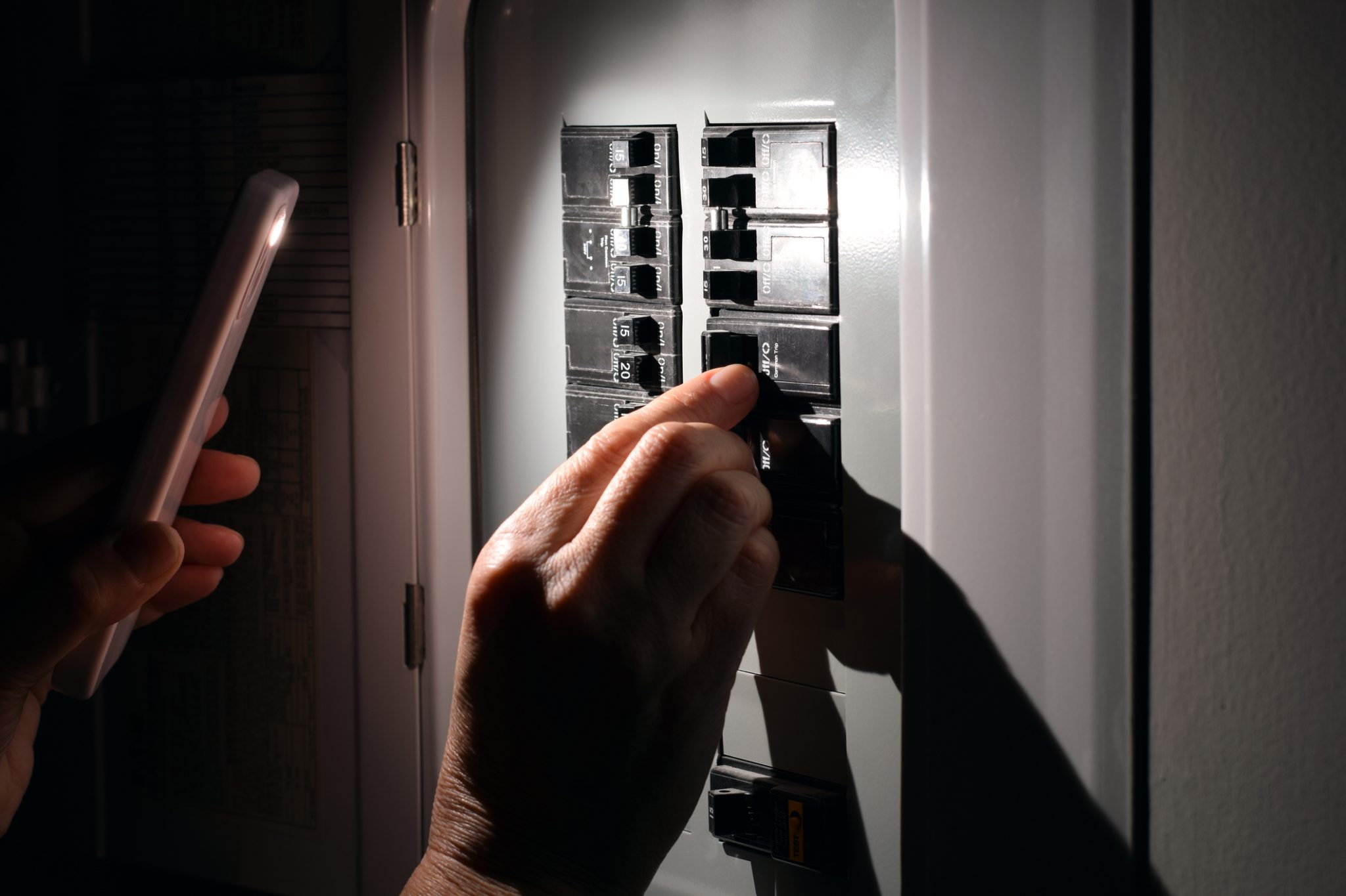 Person resetting a tripped circuit breaker on their home electrical panel during an Arizona power outage.